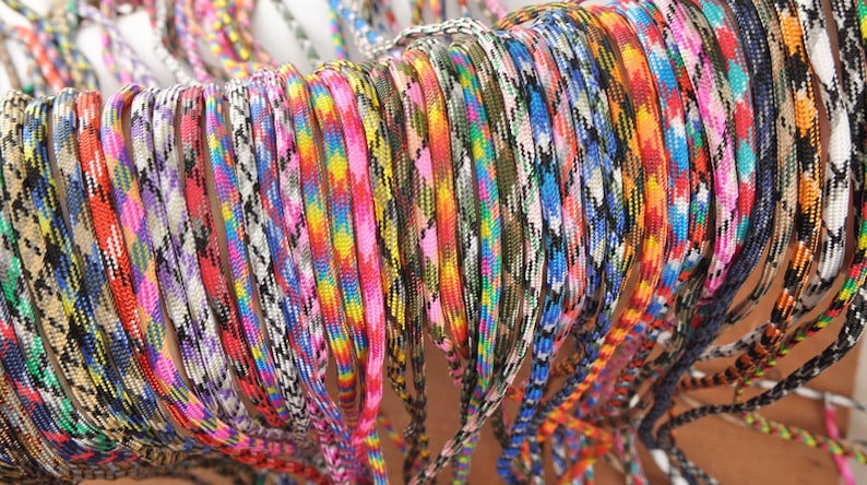 May include: A collection of colorful paracord lanyards in various patterns. The lanyards display a range of colors, including pink, blue, yellow, and green. The cords are tightly woven, creating a textured appearance. The image showcases a variety of designs.