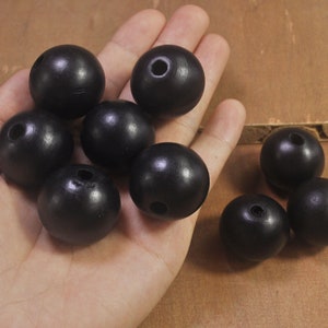 May include: A close-up of nine black wooden beads. The beads are round and have a smooth, glossy finish. They are arranged in a hand, with some beads overlapping.