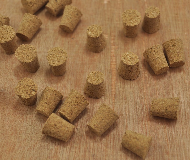 May include: A collection of cork bottle stoppers in various sizes and shapes, all made of natural cork. The stoppers are arranged on a wooden surface.