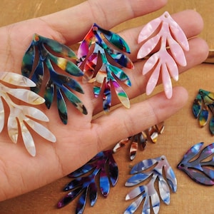 Puede incluir: Surtido de abalorios de hoja de acrílico de colores con un agujero en la parte superior para colgar. Los abalorios son de varios colores, incluyendo rosa, blanco, azul, verde y morado.