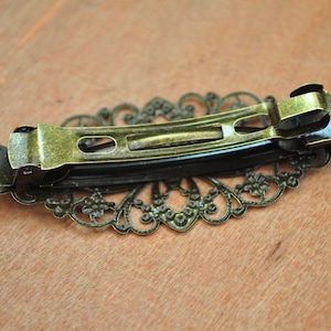 May include: A gold-toned metal hair clip with a decorative filigree design. The clip is open and ready to be used.