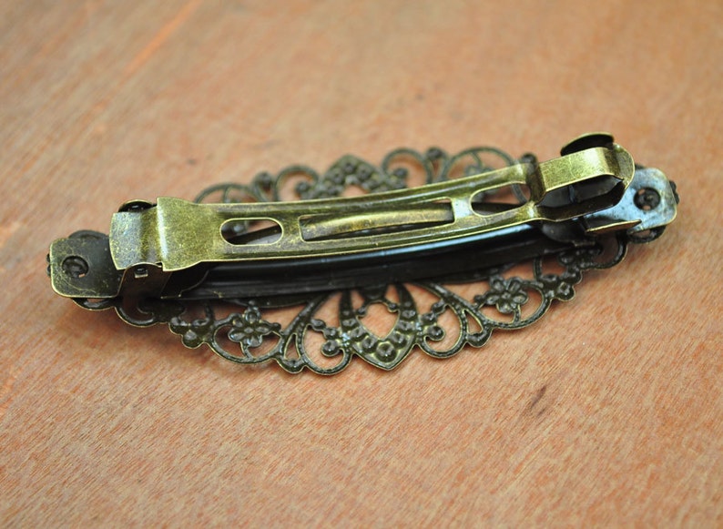 May include: A gold-toned metal hair clip with a decorative filigree design. The clip is open and ready to be used.
