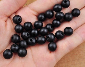 May include: A collection of black wooden beads, scattered on a hand. The beads are round and smooth, with a small hole in the center.