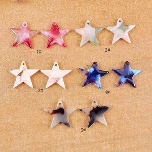 Puede incluir: Diez abalorios de resina en forma de estrella con diferentes patrones de colores. Los abalorios están dispuestos en dos filas de cinco. Los abalorios están numerados del 1 al 5.