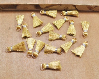 May include: A collection of 17 gold tassel trims with silver accents. The tassels are arranged on a wooden surface.