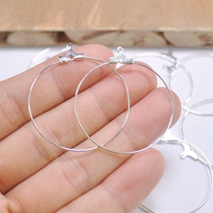 May include: Two silver hoop earrings with a simple, minimalist design. The hoops are smooth and have a slightly curved shape.