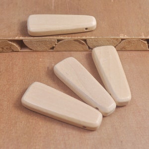 May include: Four natural wood pendant shapes, each with a hole drilled through the top. The shapes are all slightly different, but they are all roughly the same size and shape. The wood is a light brown color.
