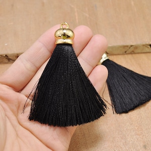 May include: Two black tassel trim with gold metal tops. The tassels are approximately 2 inches long.