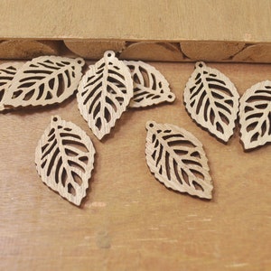 May include: A collection of eight wooden leaf-shaped embellishments with intricate cut-out designs. The leaves are a light brown color and have a smooth, polished finish.