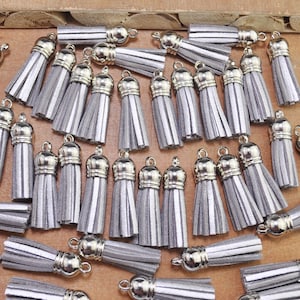 May include: A collection of silver tassel charms with silver metal tops. The tassels are made of a soft, fuzzy material and are approximately 5 cm long.