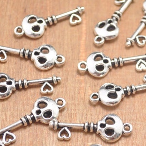 Op de afbeelding: Een groep zilverkleurige skeletsleutelbedels met hartvormige accenten. De sleutels zijn gerangschikt op een houten oppervlak.