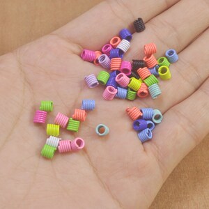 Puede incluir: Una colección de anillos de salto de metal de colores en varios tonos de rosa, azul, verde y naranja. Los anillos están dispuestos en una pila sobre una mano.