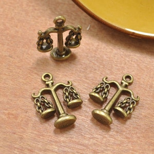 May include: Three antique gold-tone metal charms shaped like scales of justice. The charms are detailed with intricate designs and are perfect for jewelry making or crafting.