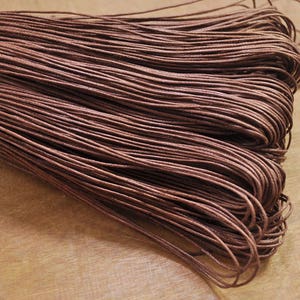 May include: A close-up of a bundle of brown waxed cotton cord. The cord is tightly wound and has a smooth, polished finish.