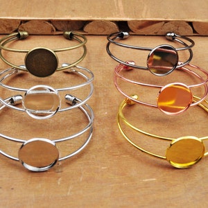 Peut inclure: Six bracelets-joncs métalliques de différentes finitions : laiton antique, canon de fusil, argent, or rose et or. Chaque bracelet est doté d'un sertissage rond pour des créations personnalisées. Les bracelets sont présentés sur une surface en bois.