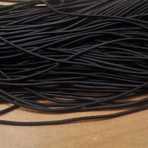 Könnte beinhalten: Nahaufnahme eines Haufens schwarzer Gummischnur. Die Schnur ist eng gewickelt und wirkt glatt. Das Bild ist gut beleuchtet und hebt die Textur und Farbe der Schnur hervor. Diese Gummischnur eignet sich für verschiedene Bastel- und Nähprojekte.