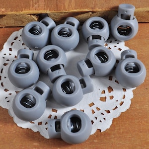 May include: Ten gray plastic toggle clasps with a spring mechanism. The clasps are round and have a hole in the center.