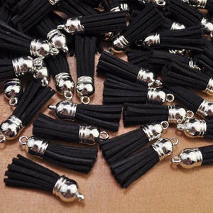 Peut inclure: Un ensemble de pompons en suédine noire avec des capuchons en métal argenté et de petites boucles. Ces pompons décoratifs sont adaptés à la fabrication de bijoux, à l'artisanat ou à l'embellissement d'articles. Les pompons sont denses.