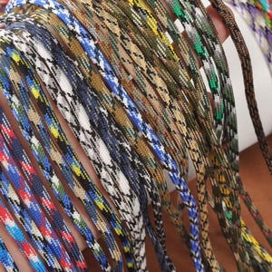 May include: A collection of colorful paracord ropes in various patterns and colors, including blue, red, white, and camouflage designs. The ropes are tightly woven and appear durable, suitable for crafting or outdoor use.