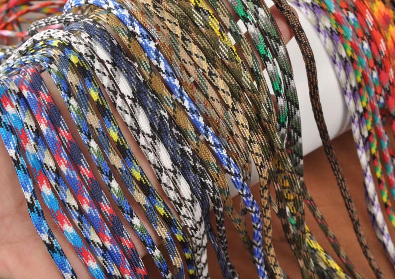 May include: A collection of colorful paracord ropes in various patterns and colors, including blue, red, white, and camouflage designs. The ropes are tightly woven and appear durable, suitable for crafting or outdoor use.