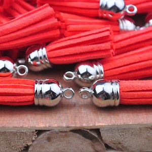 May include: A group of red tassel keychains with silver metal caps. The tassels are made of a soft, fuzzy material and are attached to a silver metal ring.
