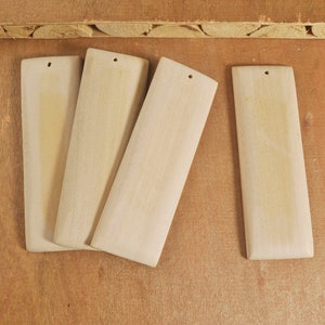 May include: Four rectangular wooden pieces with rounded edges and a hole in the centre. The pieces are light brown in colour and are arranged in a row on a wooden surface.