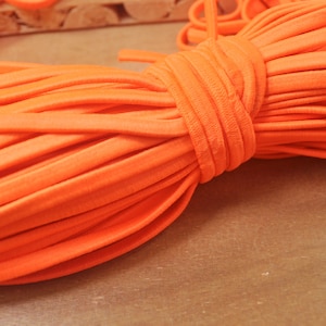 Può includere: Un primo piano di un fascio di cordoncino elastico arancione brillante. Il cordoncino è morbido e flessibile, ed è perfetto per progetti di artigianato.