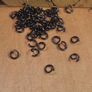 Puede incluir: Un montón de anillos de salto de metal negro, esparcidos sobre una superficie de madera. Los anillos son pequeños y redondos, con un acabado liso.
