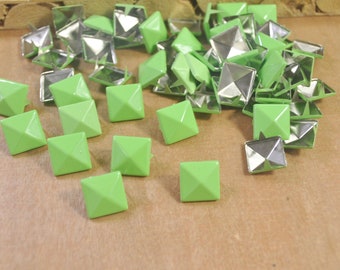 Puede incluir: Una colección de tachuelas decorativas cuadradas de color verde lima con respaldo de metal plateado. Las tachuelas tienen un diseño piramidal y están dispersas sobre una superficie. Estas tachuelas decorativas son ideales para proyectos de manualidades.