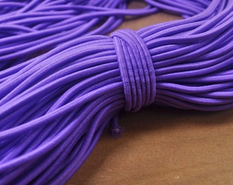 Peut inclure: Gros plan d'un gros paquet de cordon élastique violet. Le cordon est enroulé serré et a une finition lisse et brillante.