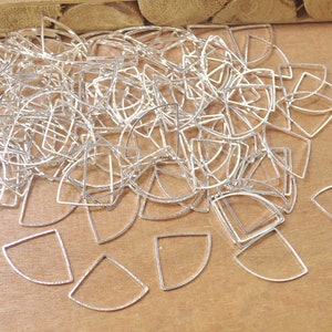 May include: A pile of silver-toned metal half-circle and square shapes. The shapes are all the same size and are arranged in a random pattern. The shapes are on a wooden surface.