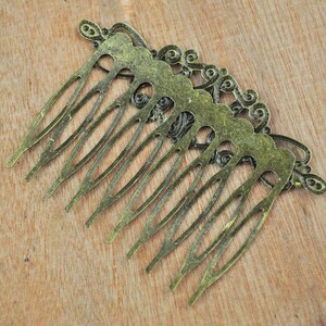May include: A vintage-style hair comb with an ornate design. The comb is made of metal and has a gold finish. It has a decorative, scalloped edge and a series of teeth.