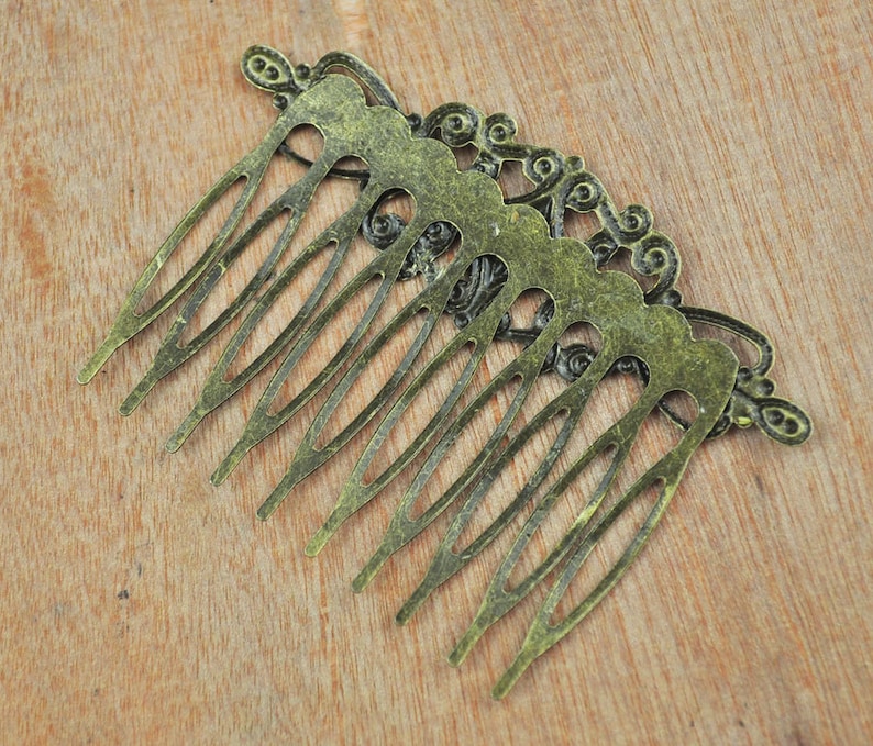 May include: A vintage-style hair comb with an ornate design. The comb is made of metal and has a gold finish. It has a decorative, scalloped edge and a series of teeth.