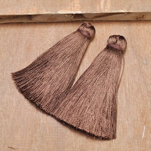May include: Two brown silk tassels with a long fringe. The tassels are made of soft, silky material and have a delicate, elegant look.