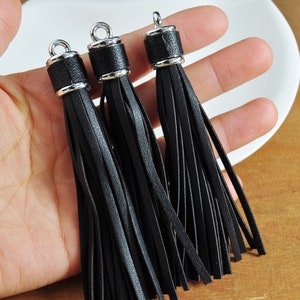 May include: Three black leather tassels with silver metal tops. The tassels are hanging from a hand.