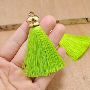 May include: Two lime green silk tassels with gold metal caps. The tassels are approximately 2 inches long.