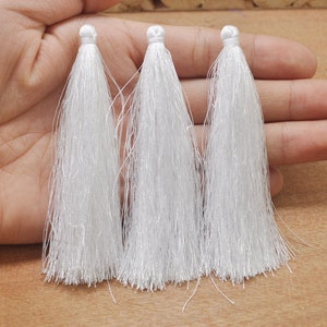 May include: Three white tassel trims, each with a knotted top and long, flowing strands.