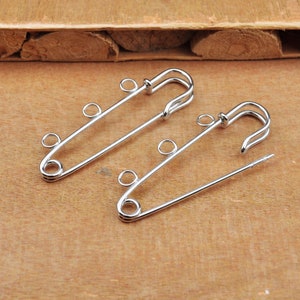 May include: Two silver safety pins with multiple loops for attaching jewelry or other items.