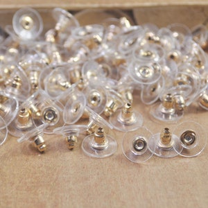 May include: A large pile of clear plastic earring backs with gold-colored metal posts.