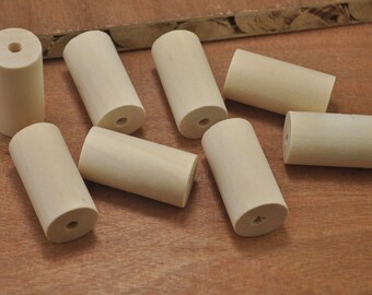 Peut inclure: Huit chevilles en bois, chacune avec un trou percé au centre. Les chevilles sont de couleur brun clair et sont disposées de manière dispersée sur une surface en bois.