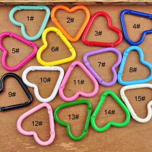 May include: A collection of colorful metal carabiner clips in various shapes, including hearts and triangles. The clips are in shades of blue, orange, red, pink, yellow, purple, green, black, and white. Each clip is numbered.