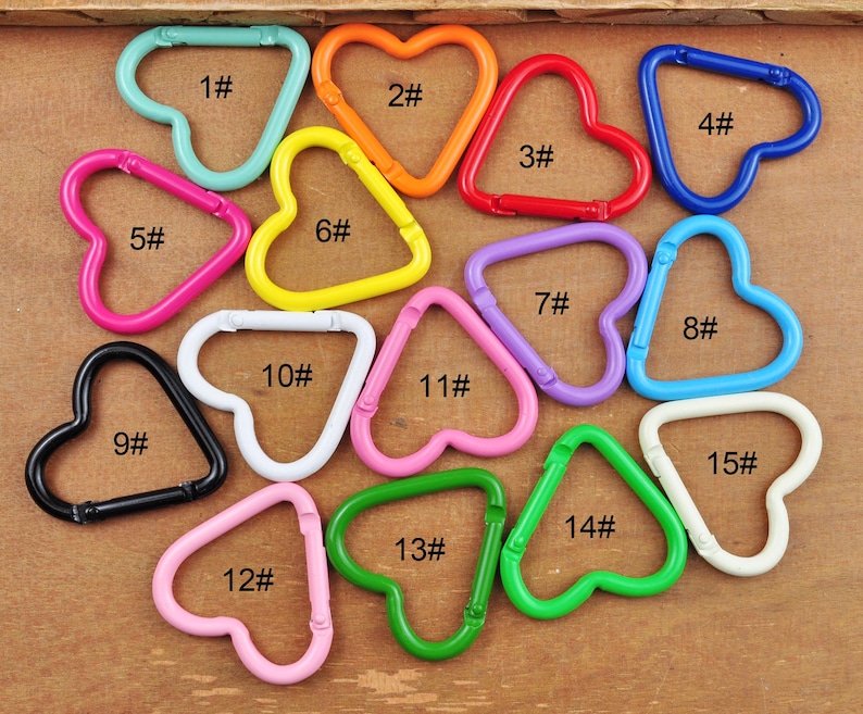 May include: A collection of colorful metal carabiner clips in various shapes, including hearts and triangles. The clips are in shades of blue, orange, red, pink, yellow, purple, green, black, and white. Each clip is numbered.