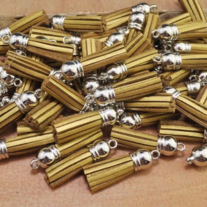 May include: A large group of gold leather tassels with silver metal caps. The tassels are arranged in a pile, with some of them overlapping.