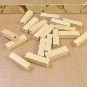 Könnte beinhalten: Ein Haufen natürlicher Holzstiftchen mit einem Loch, das durch die Mitte jedes Stiftchens gebohrt ist. Die Stiftchen sind auf einer hellbraunen Oberfläche verstreut.
