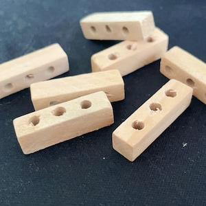 Può includere: Sei blocchi di legno, ognuno con quattro fori. I blocchi sono di colore marrone chiaro e hanno una finitura liscia.
