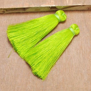 May include: Two lime green tassel trims with a knotted top. The tassels are made of soft, silky threads.