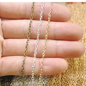 Puede incluir: Tres hebras de cadena en colores dorado, plateado y bronce. Las cadenas se sostienen en una mano, y el fondo es una pila de cadenas similares.