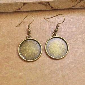 May include: A pair of round, gold-toned metal earrings with a simple hook design. The earrings have a smooth, slightly textured surface.