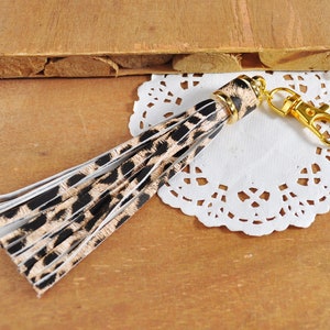 May include: A gold key chain with a black and brown leopard print tassel.