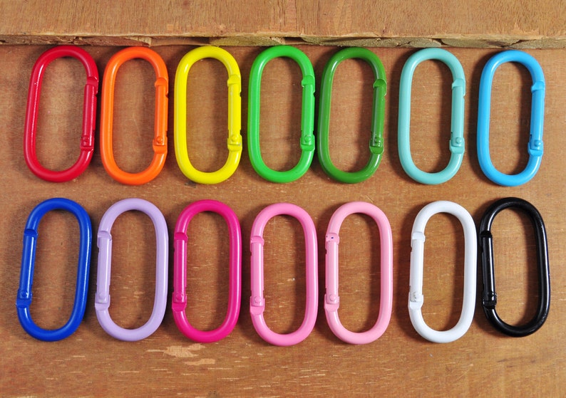 May include: A set of 12 colorful oval-shaped metal keychains. The keychains are arranged in a rainbow pattern, with each keychain a different color. The keychains are all the same size and shape.